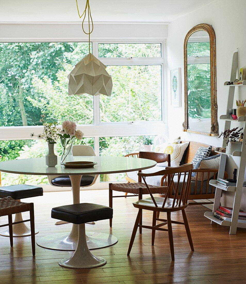 Tulip table, matching stools and wooden chairs in contemporary interior with view of garden