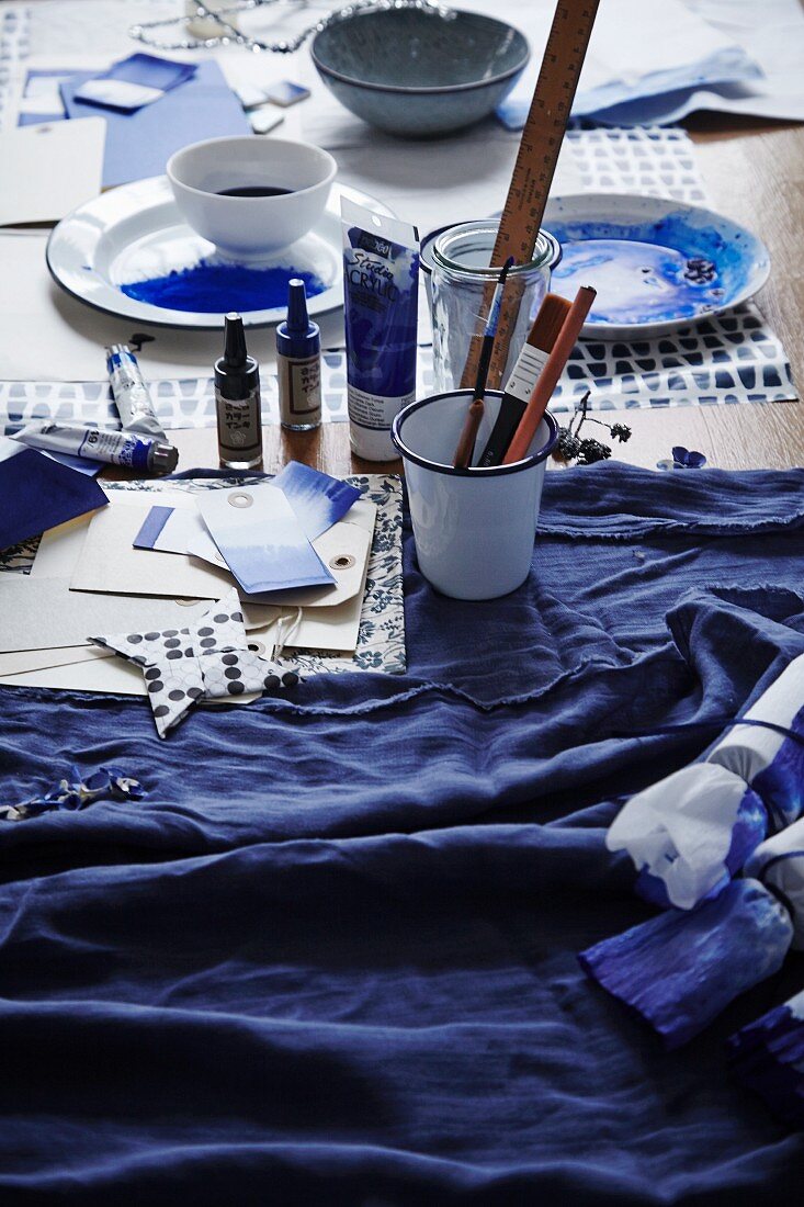 Dyed fabrics, papers, containers of indigo dye and painting utensils on craft table