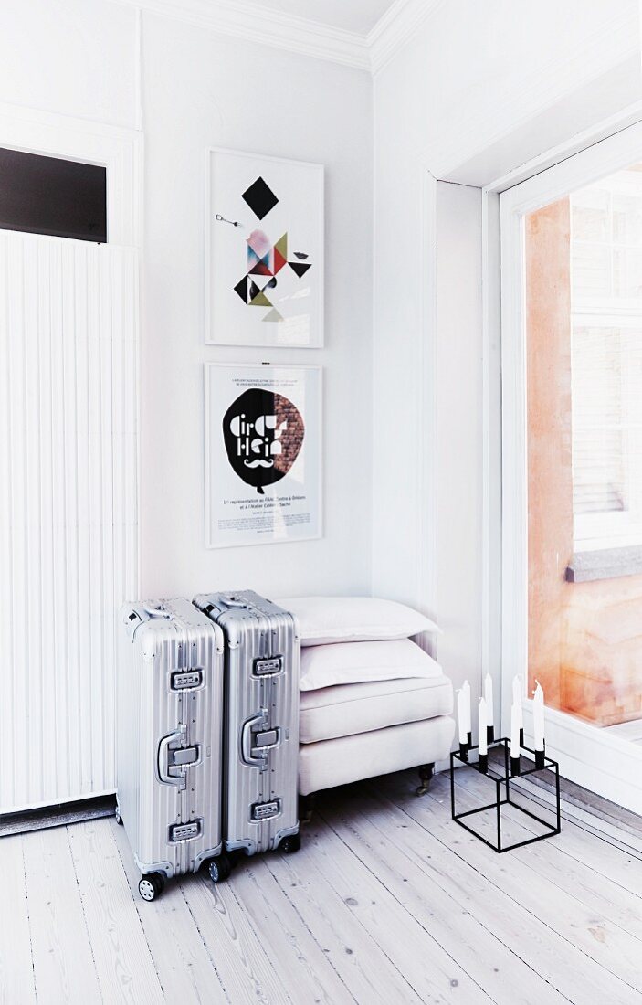 Two aluminium, wheeled suitcases below framed pictures and cubic candelabra on wooden floor
