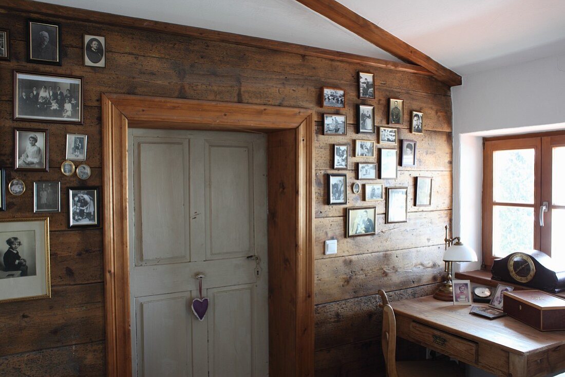 Schreibtisch vor Fenster, seitlich an Holzwand aufgehängte Familienfotos