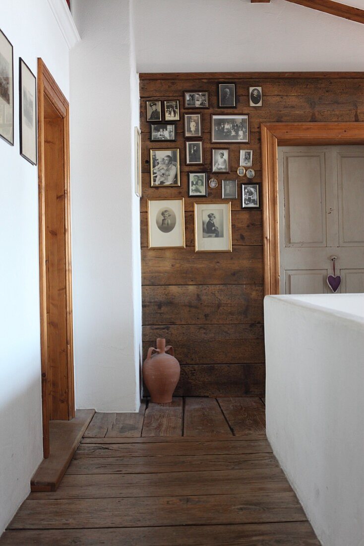 Treppenhaus, seitlich geweisselte Brüstungswand, im Hintergrund Fotosammlung an Holzwand