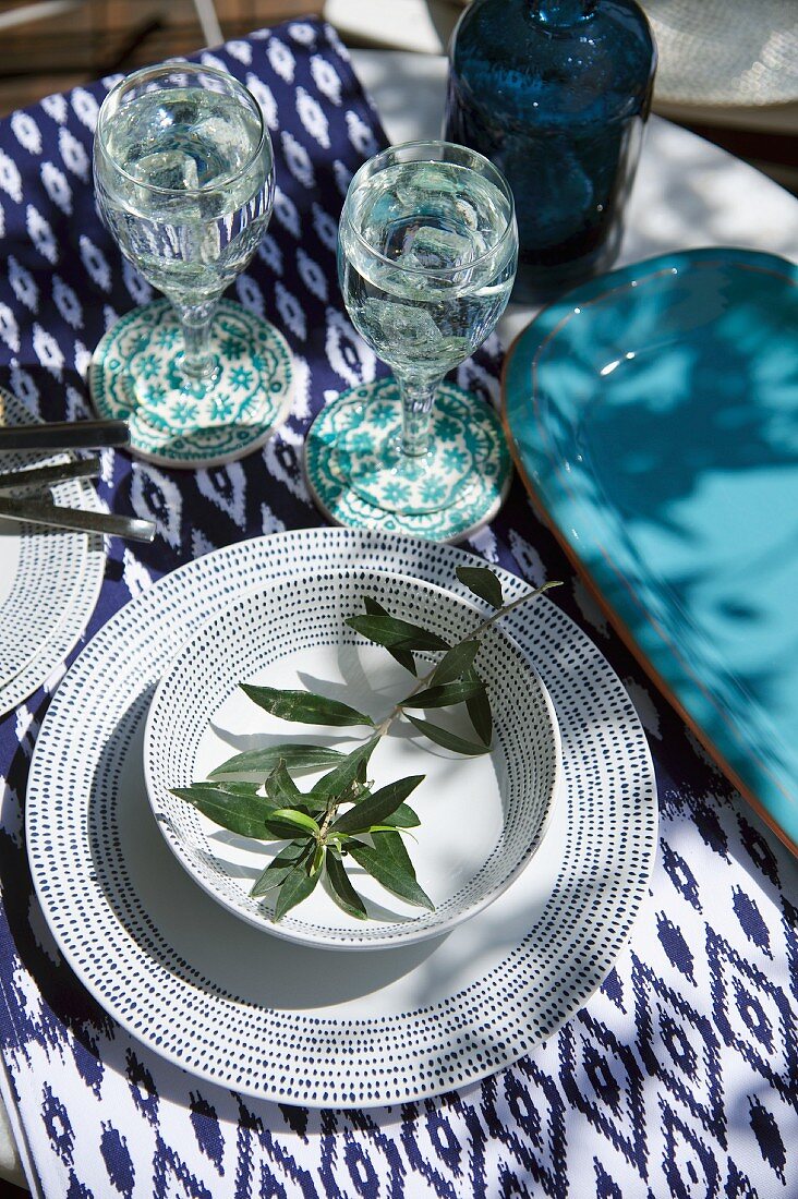 Gedeck mit weiss-blauem Muster und Olivenzweig, Ikatmuster auf Tischtuch