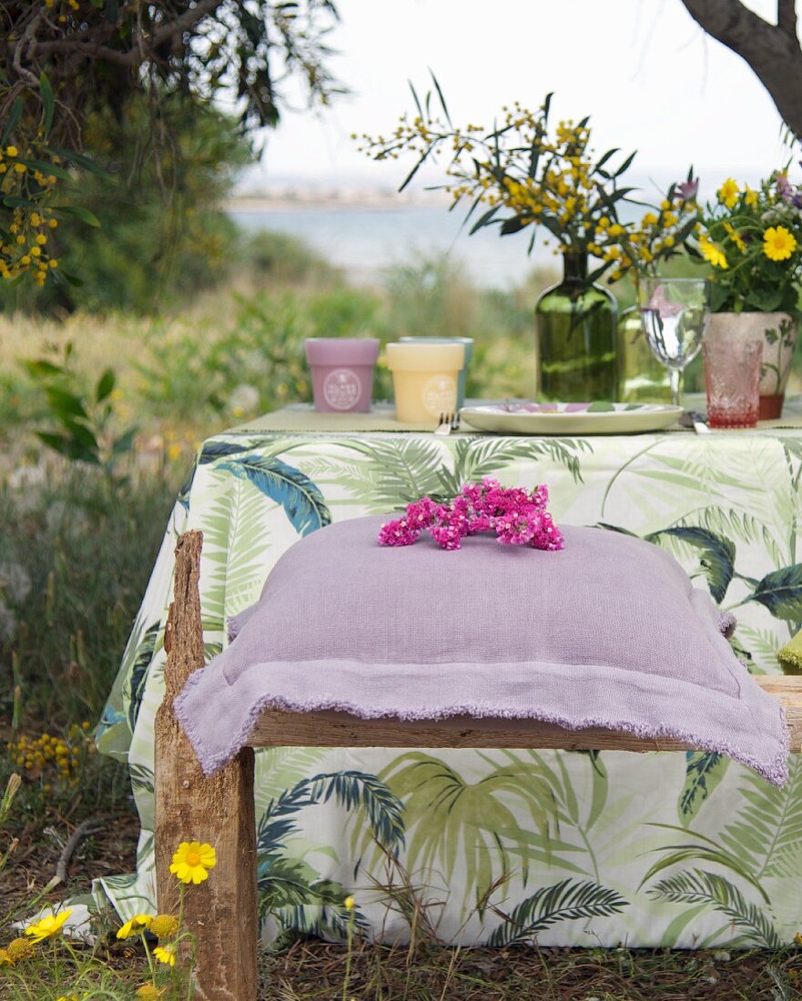 Purple linen cushion on rustic wooden bench next to set garden table