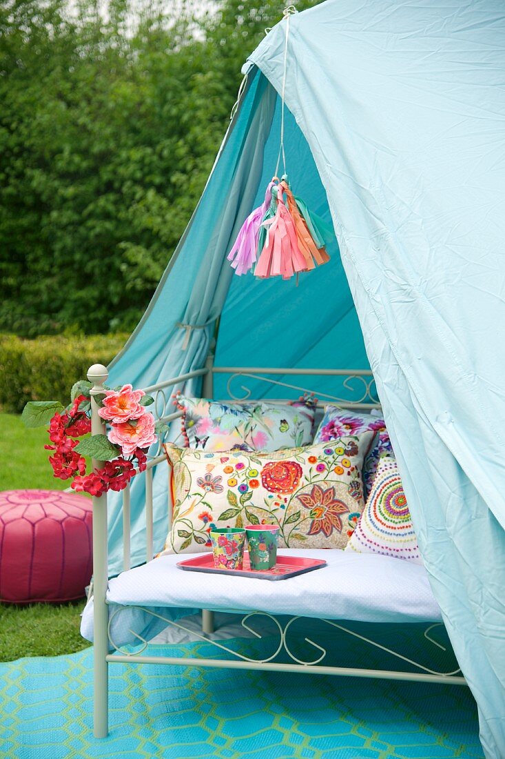 Metal bench with cushions in pale blue tent in garden