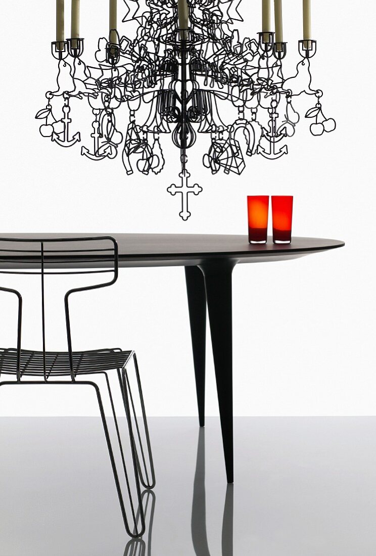Artistic metal chandelier with stylised figures and symbols hanging over designer table and wire chair