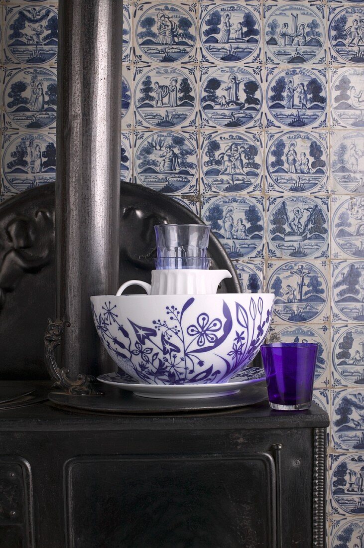 Blue and white crockery on antique cast iron stove against old wall tiles in classic Delft blue and white