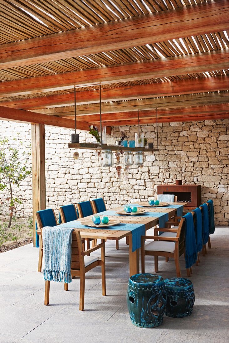 Dining area below bamboo pergola; blue blankets, lamps and tealight holders on suspended wooden board