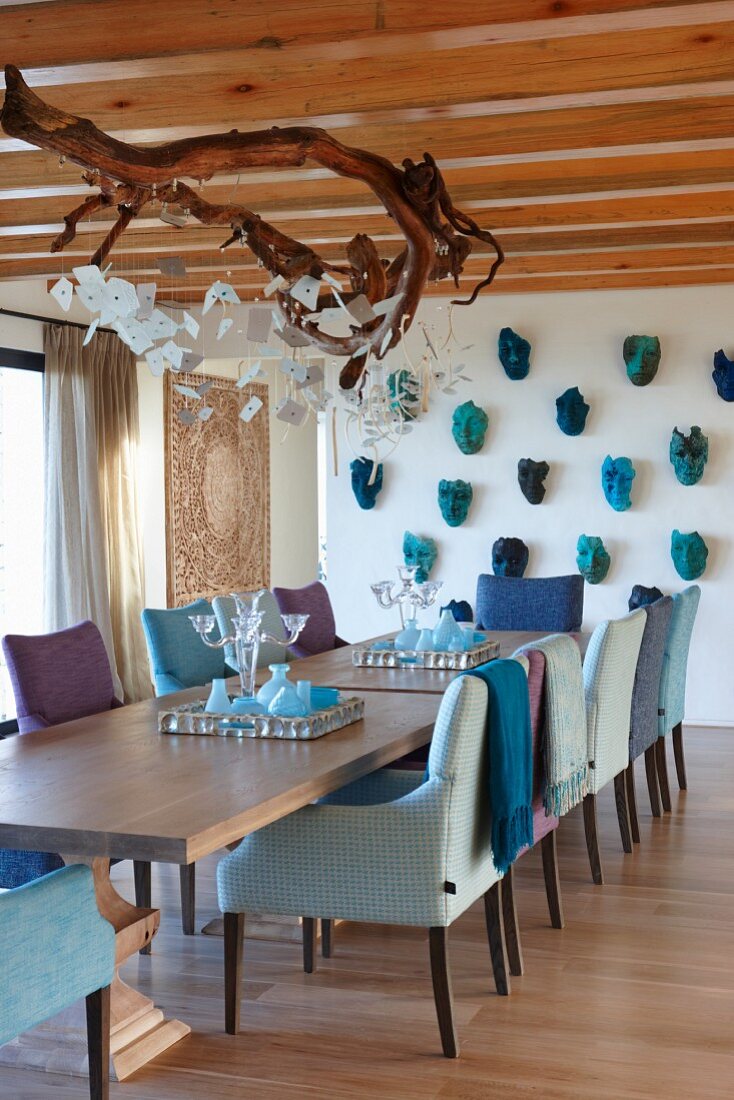 Dining room with comfortable armchairs and lamp made from branch; masks on wall, armchairs and accessories in various shades of blue