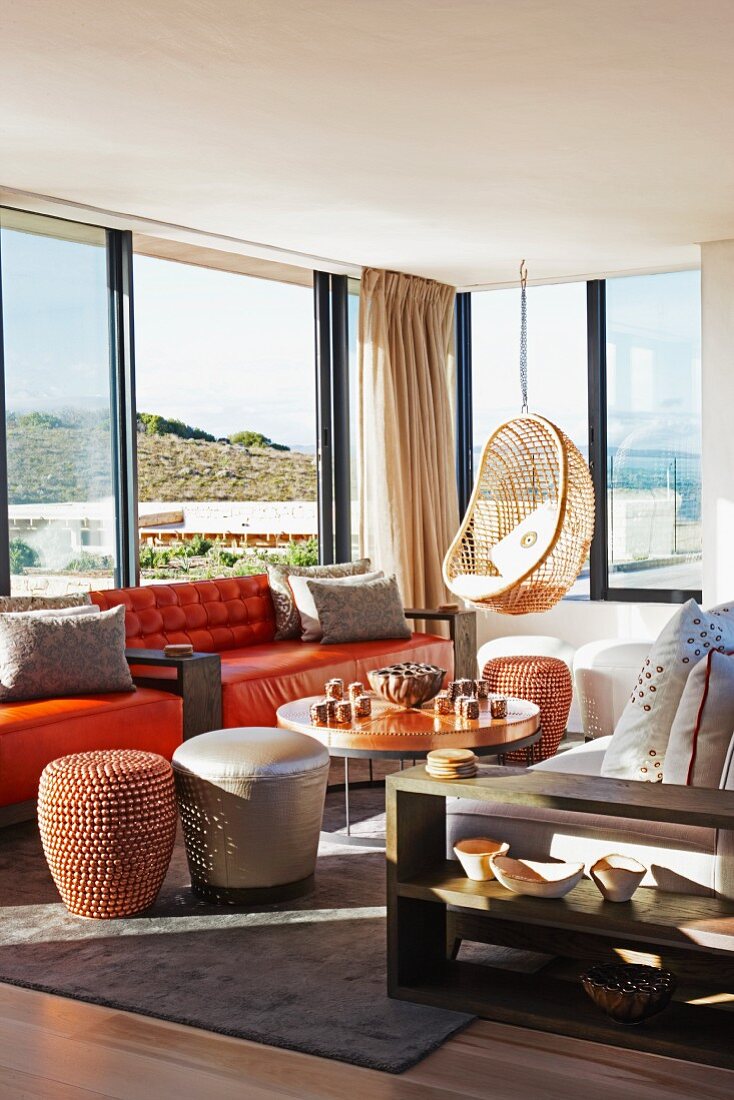 Verschiedene Sitzmöble, wie Hängesessel, Sofa und Sitzpouf im Loungebereich, Ausblick durch Panoramafenster
