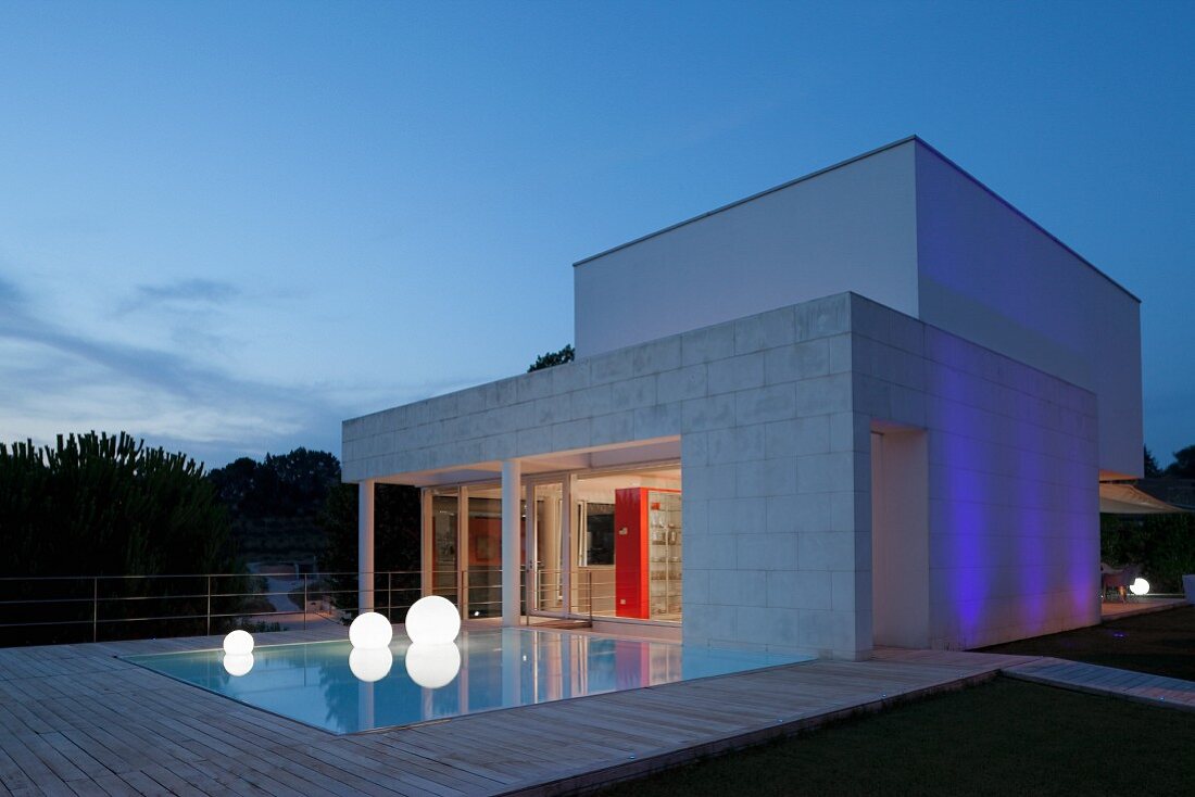 Twilight atmosphere; pool, spherical floor lamps and wooden deck outside contemporary house