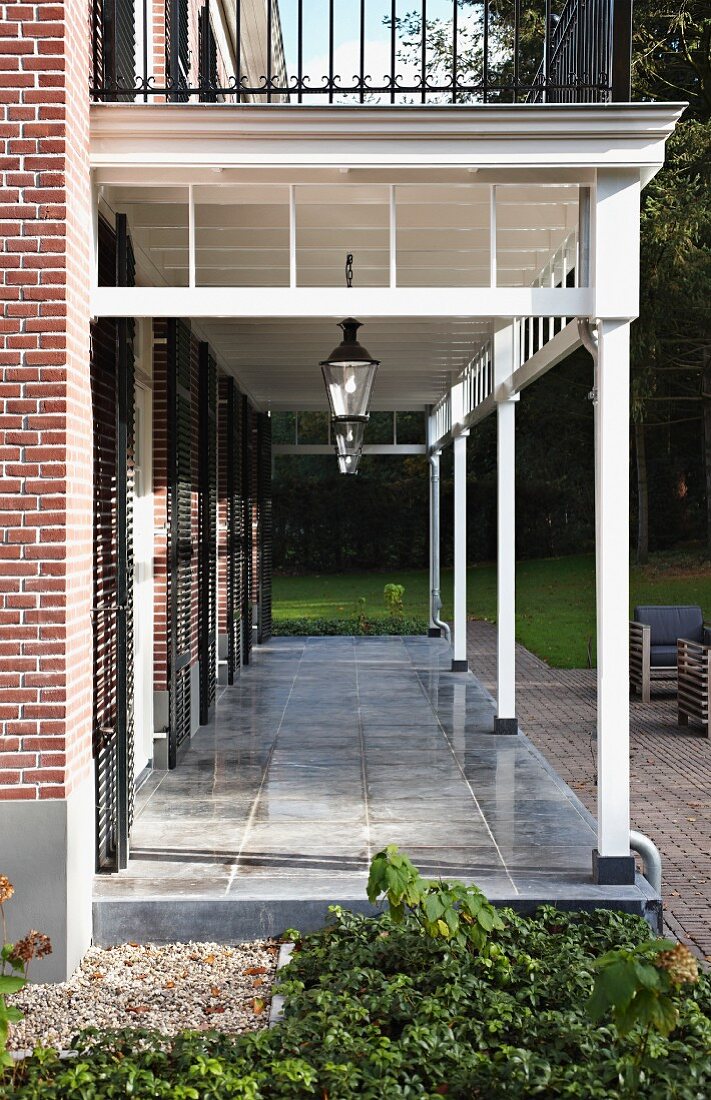 Veranda with white wooden structure and grey stone floor adjoining brick house
