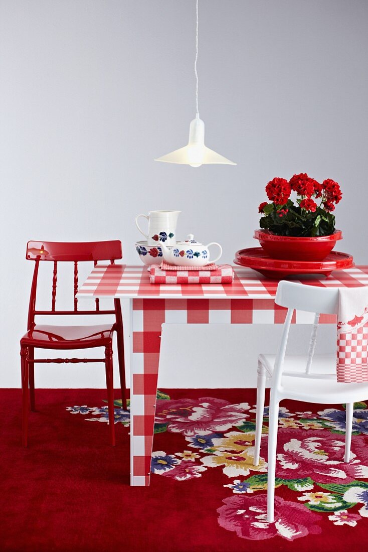 Mixture of red and white patterns; gingham table and brightly painted chairs on floral rug