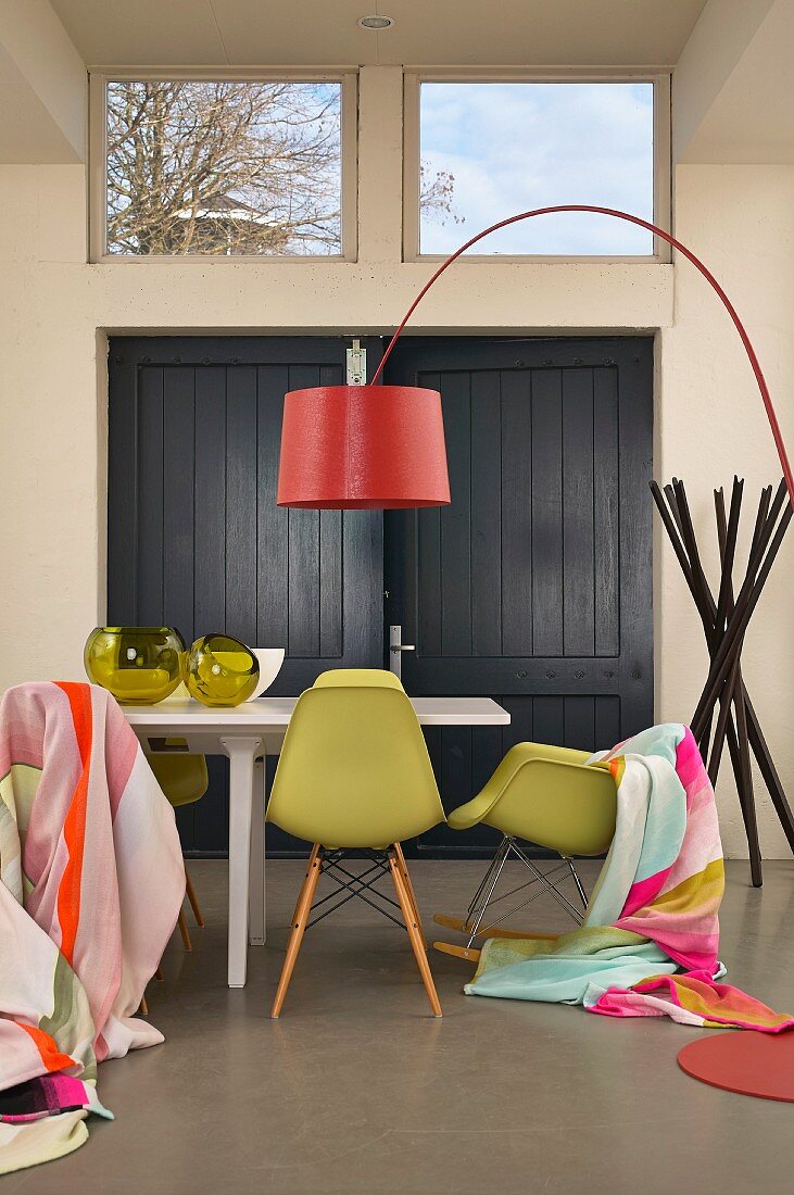 Esstisch mit drapierten Tüchern auf Klassikerstühlen, rote Designer-Bogenleuchte und Garderobenständer im Hintergrund