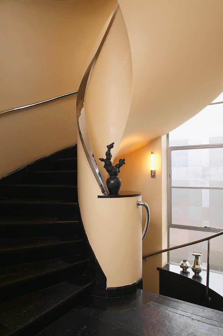 Elegant, curved staircase with black stone steps, chrome handrail and sculpture on newel