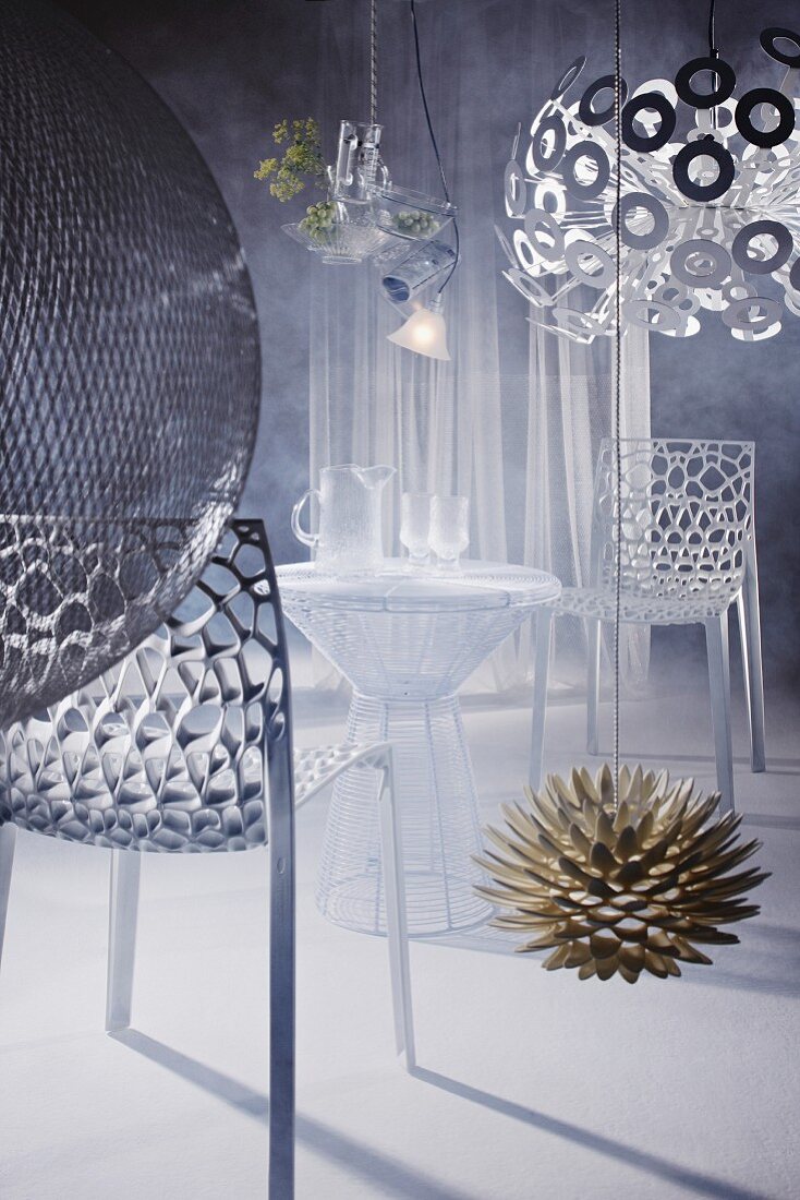 Stühle aus organisch geformten Metallstrukturen und Tisch aus Metallgewebe in geheimnisvoller Atmosphäre, umgeben von Designer-Leuchten in Blütenformen (Dandelion)