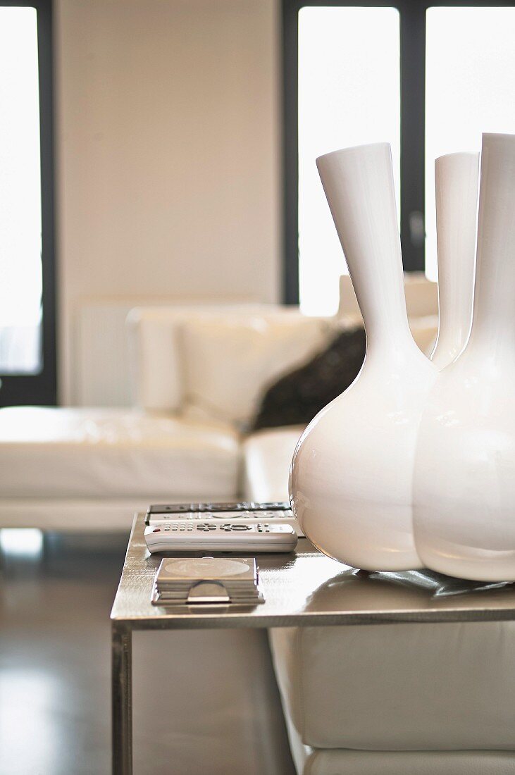 Designer-Vase mit mehreren Hälsen auf minimalistischem Stahltisch, Überecksofa unscharf im Hintergrund