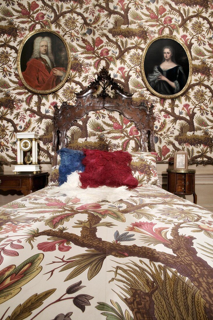 Grand bedroom with bed linen and wallpaper in matching floral pattern and oval historical portraits on wall