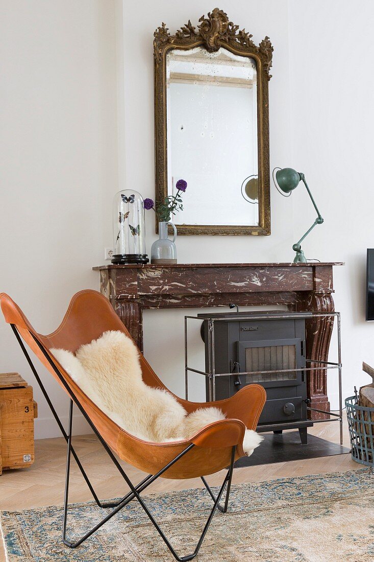 Leather Butterfly chair with sheepskin blanket in front of fireplace with marble surround, retro lamp and antique mirror