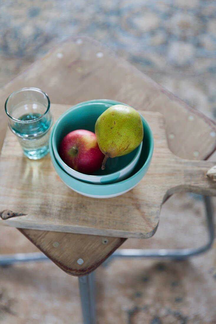 Fruit in ceramic bowls and glass of water on chopping board on side table