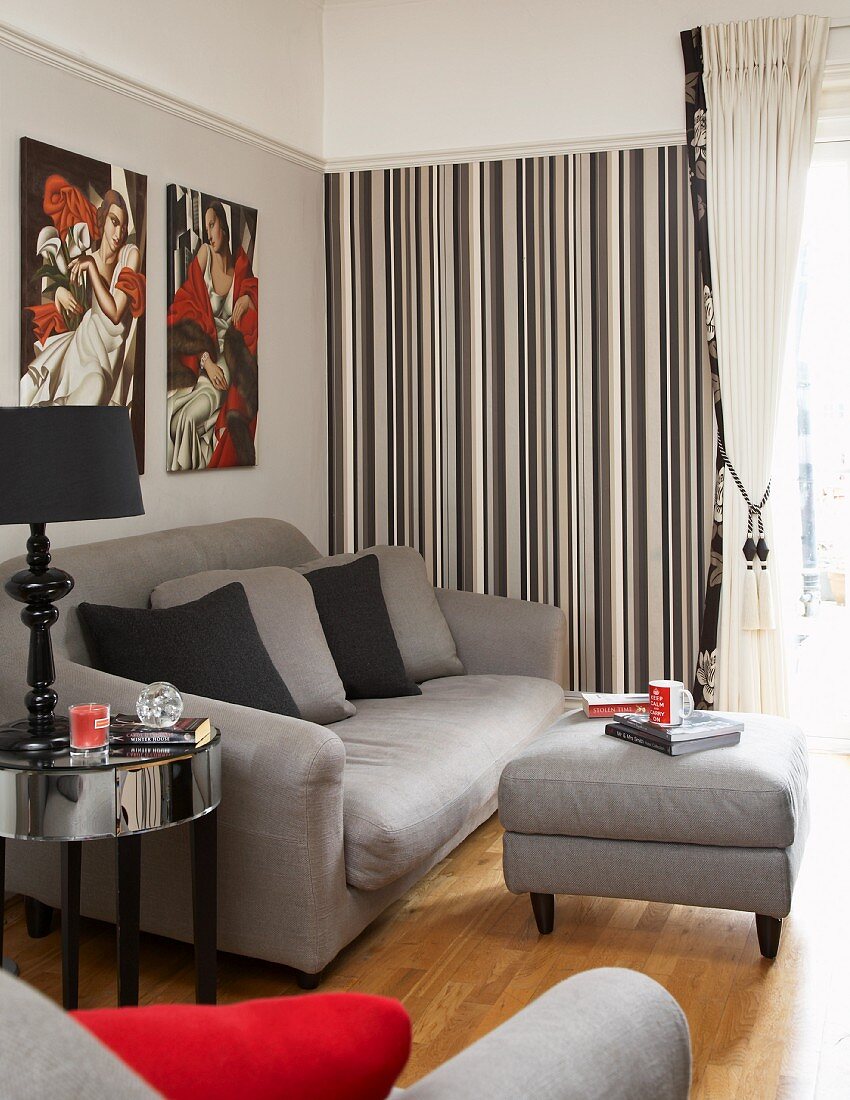 Graue Sofagrnitur mit Polsterhocker als Tisch in Wohnzimmer mit Streifentapete und grauer Wand