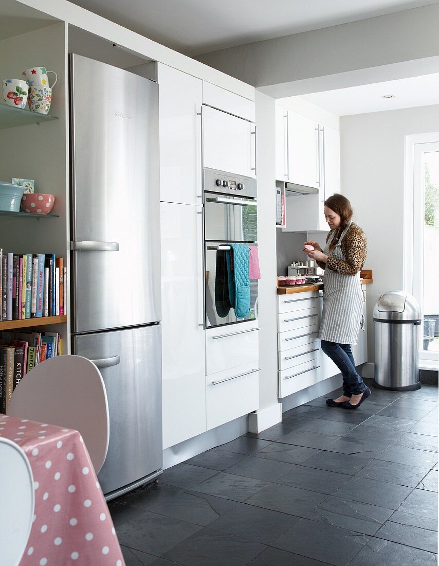 Frau im Hintergrund in zeitgenössischer Küche, weiße Einbauschränke und integrierter Kühlschrank aus Edelstahl