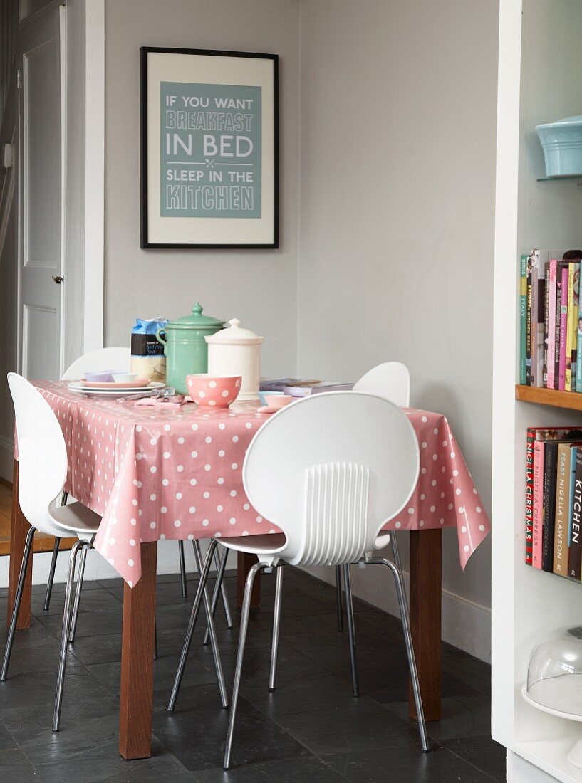 Essplatz in hellgrau getönter Küchenecke, weiße Kunststoff Stühle um Tisch mit rosa Tischdecke