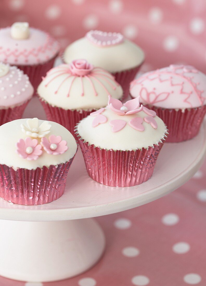 Verzierte Muffins in rosa Förmchen auf weisser Etagere
