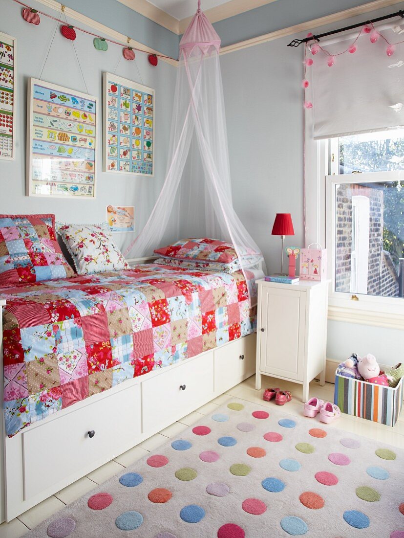 Bunter Punkte-Teppich vor Bett mit Schubladen und Patchworkdecke in hellblau getöntem Kinderzimmer