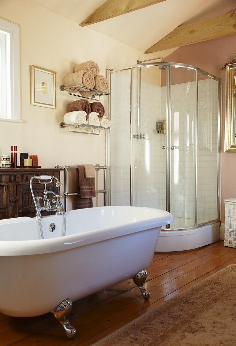 Freistehende Badewanne und moderne Duschkabine in einem Wohnbad mit Antikkommode und Orientteppich auf dem Dielenboden