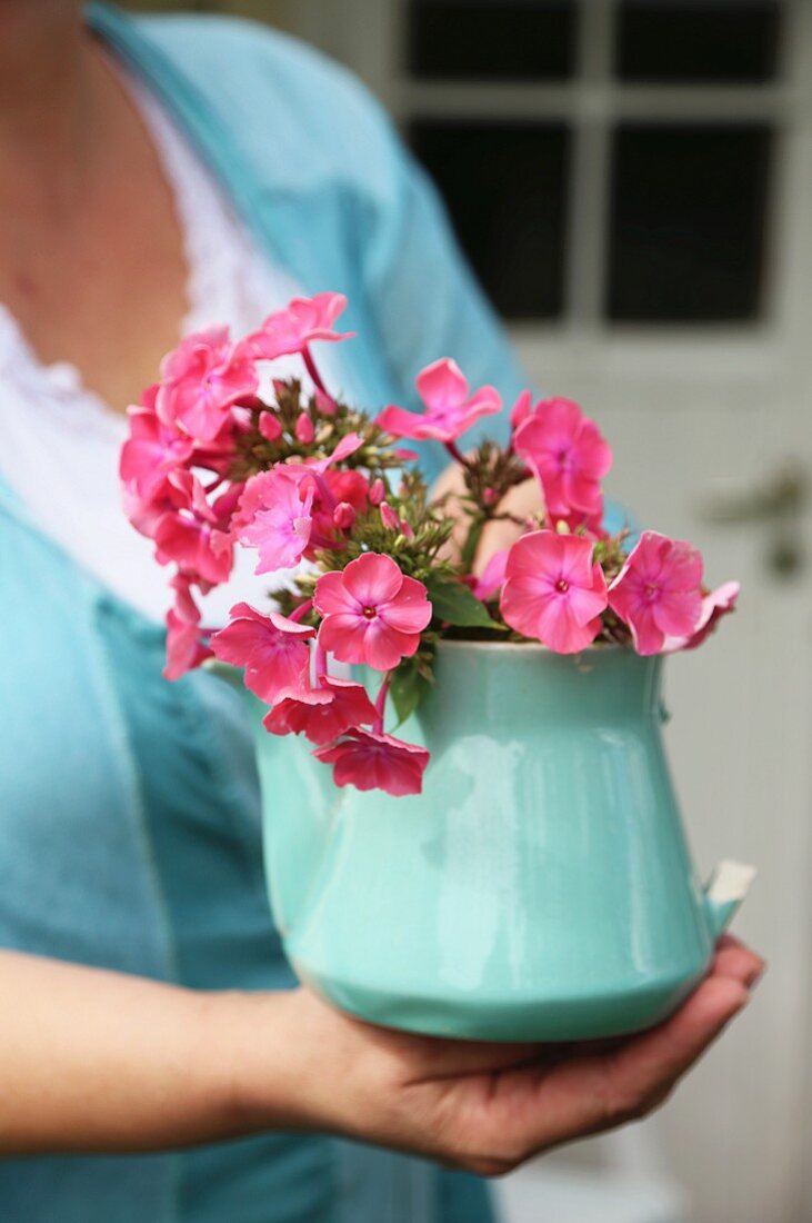 Pink phlox flowers in vintage, turquoise teapot held in woman's hands