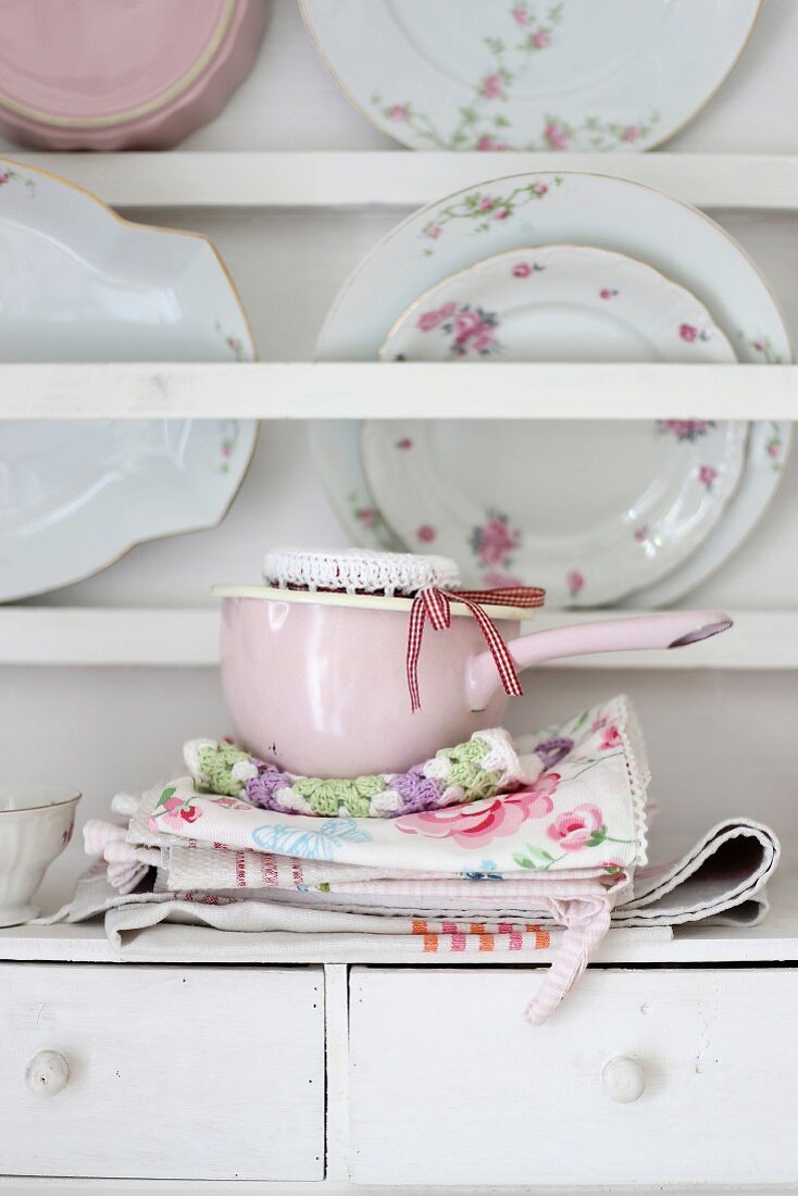 Rosa Stielkasserolle auf geblümtem Küchentüchern und Wandboard mit Vintage Tellern