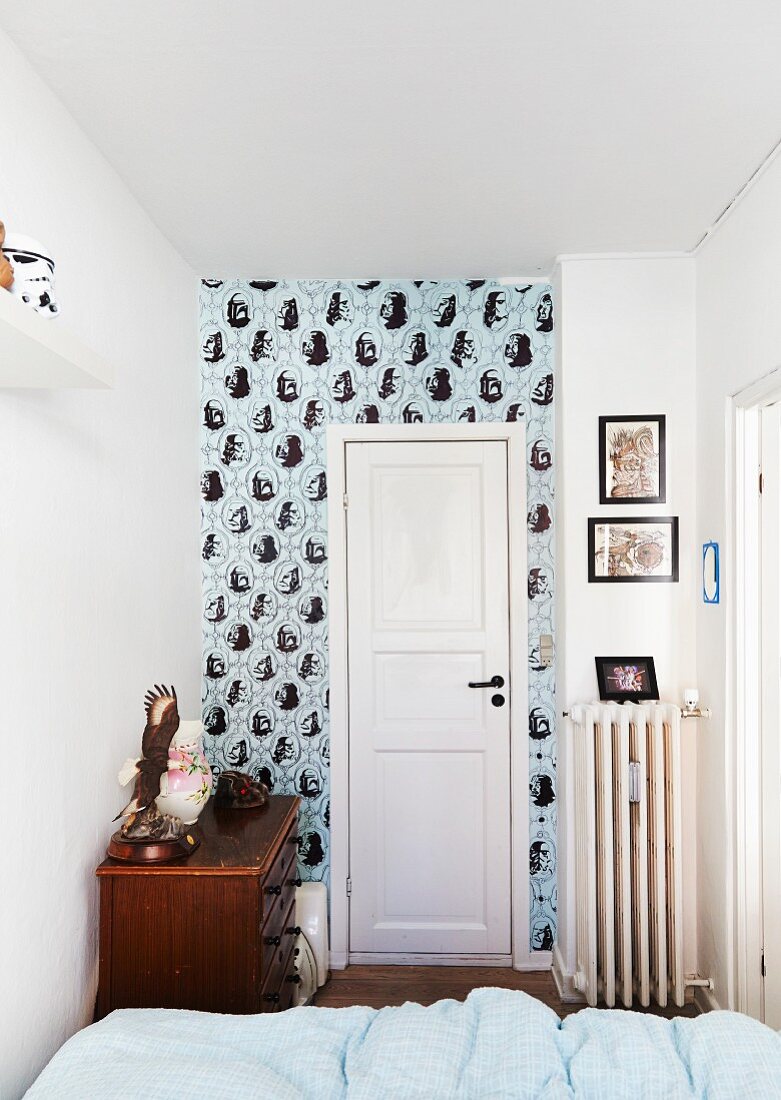 Blick über Bett auf weiße Zimmertür und tapezierte Wand in schmalem Raum