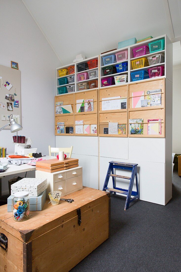 Storage boxes on top of wooden trunk and colourful baskets on partition shelving in study