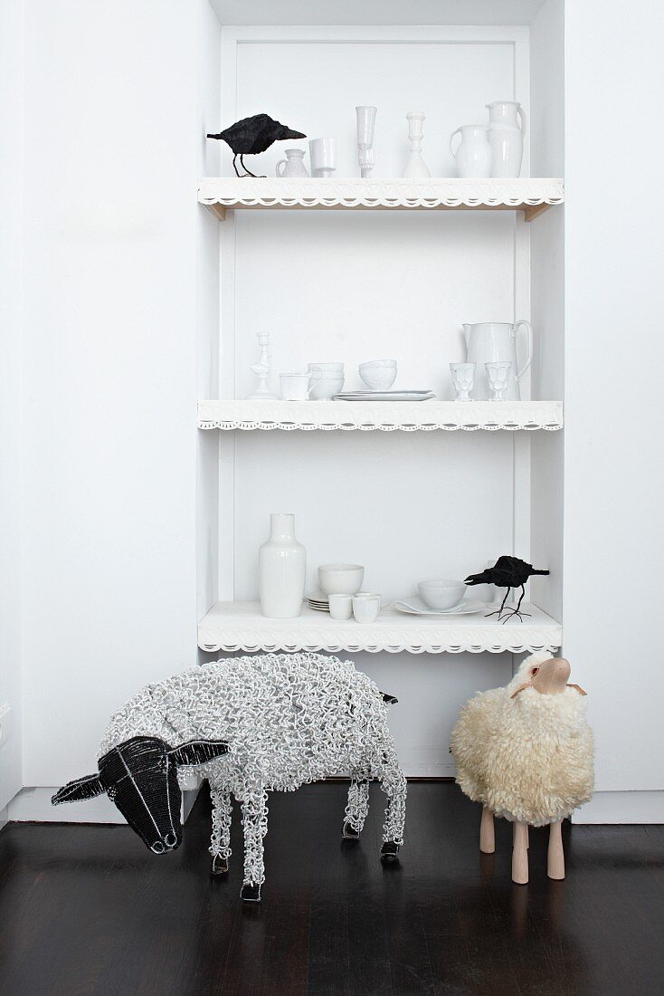 Figurines of birds and crockery on shelving in niche behind sheep sculptures