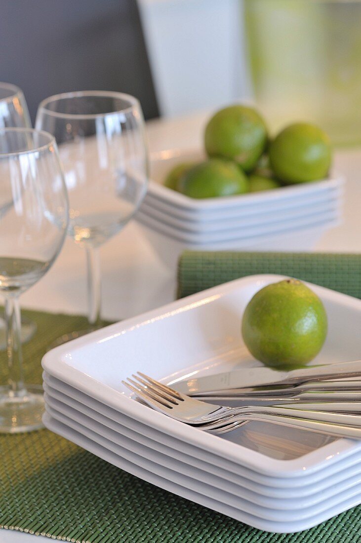 Lime and cutlery on stacked plates next to wine glasses