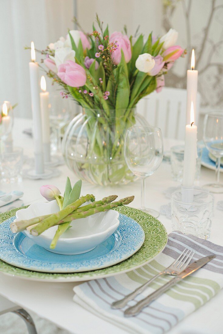 Pastellfarbenes Gedeck mit Spargelstangen und Tulpenstrauss in Glasvase auf festlich gedecktem Tisch