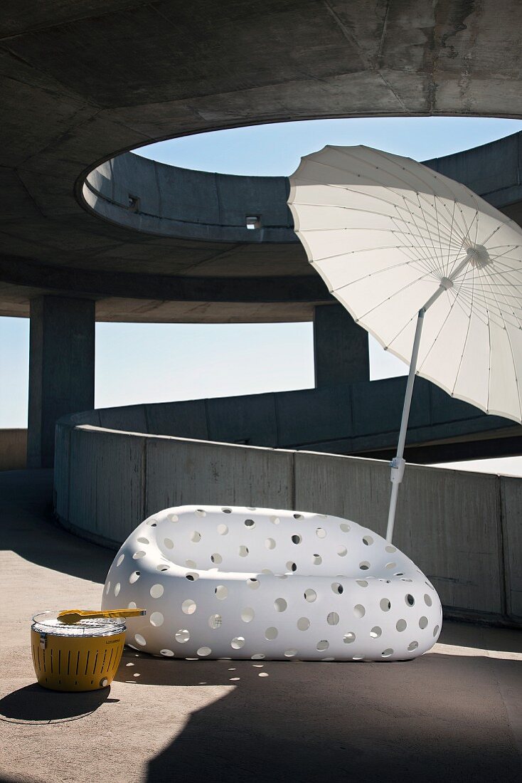 Designer-Outdoor-Sofa aus weißem Kunststoff mit Lochmuster und asiatischer Sonnenschirm auf sonniger Betonrampe