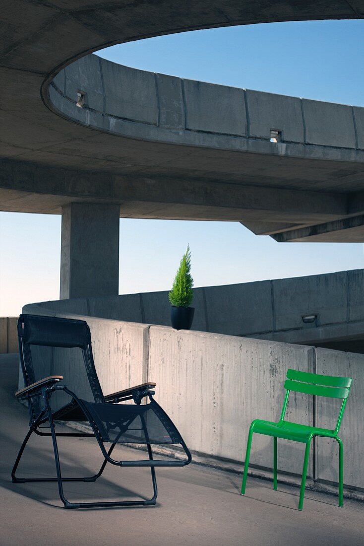 Metal tube lounger with mesh seat and grass green outdoor chair on ramp of concrete building