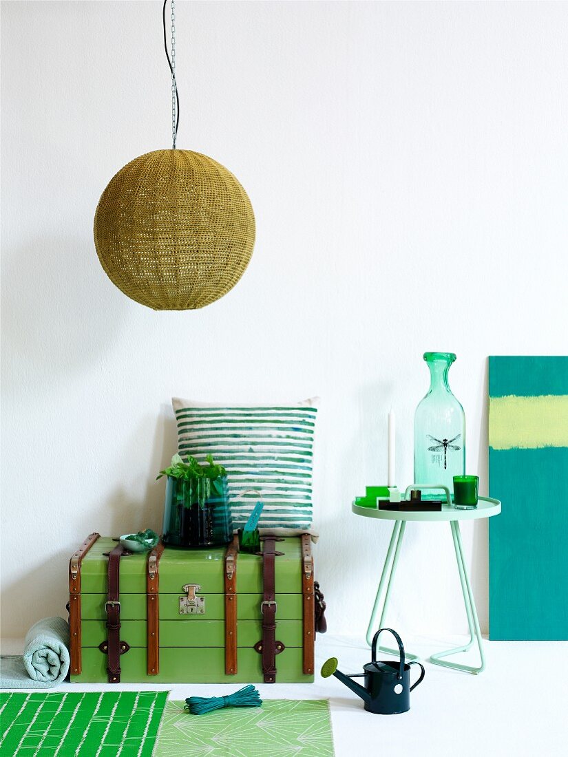 Arrangement in shades of green - pendant lamp with wicker lampshade, steamer trunk and ornaments on side table
