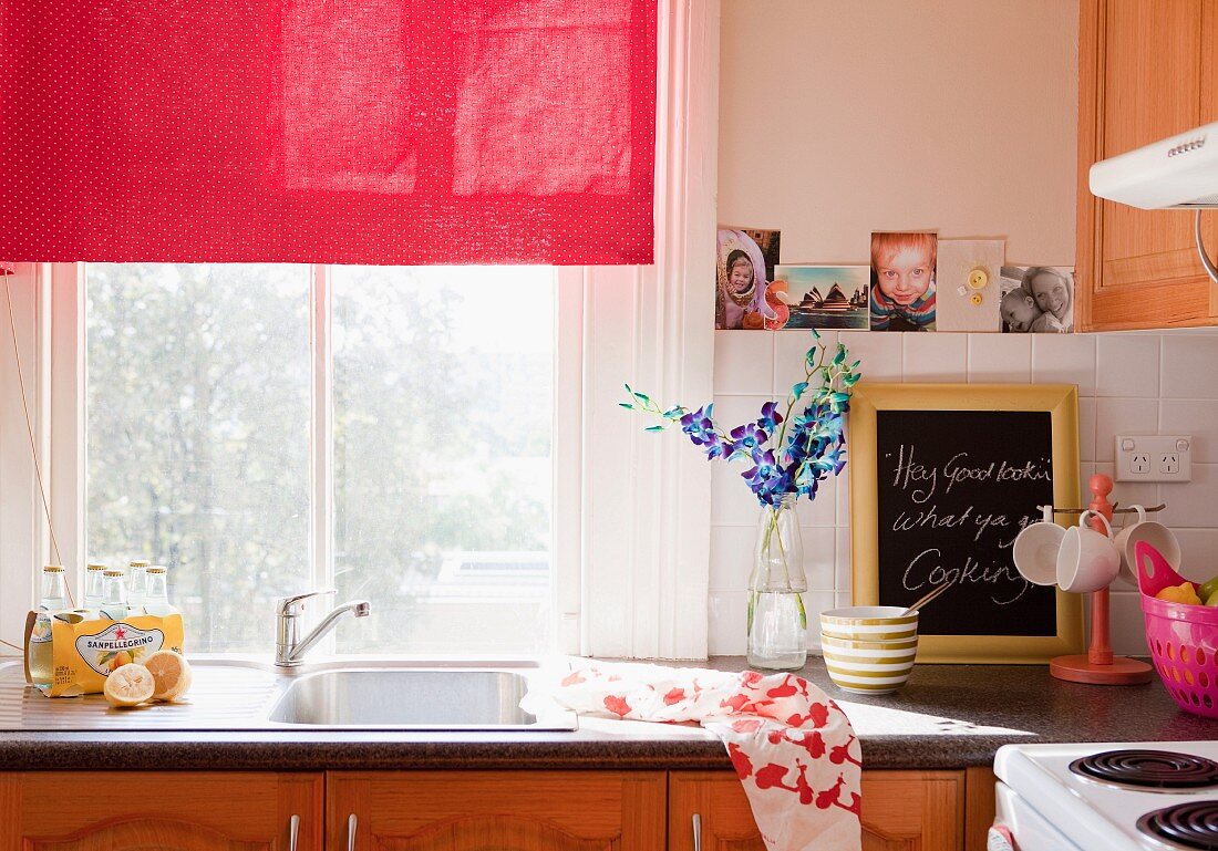Fenster mit rotem Stoffrollo über Edelstahlspüle in romantisch dekorierter Küche mit Holzfronten