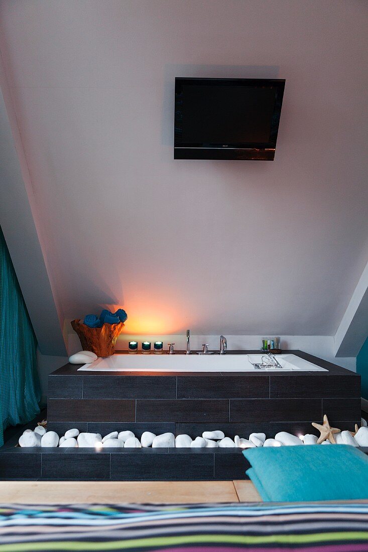 Bathtub with dark-tiled front under sloping ceiling