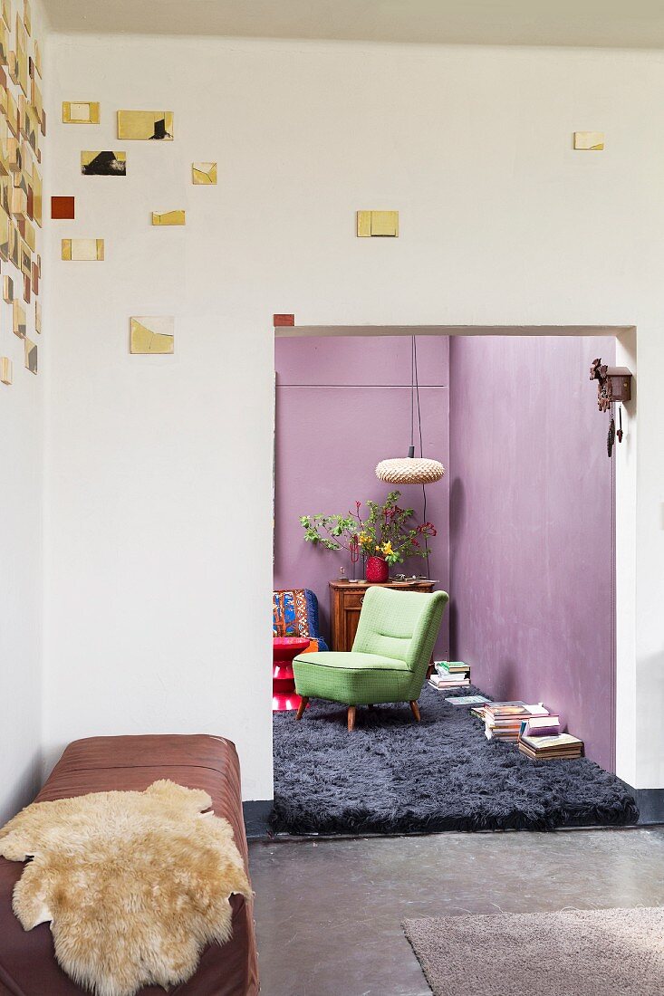 Künstlerische Wanddekoration über Bank mit Tierfell in Raumecke; Blick ins Wohnzimmer mit lila Wänden