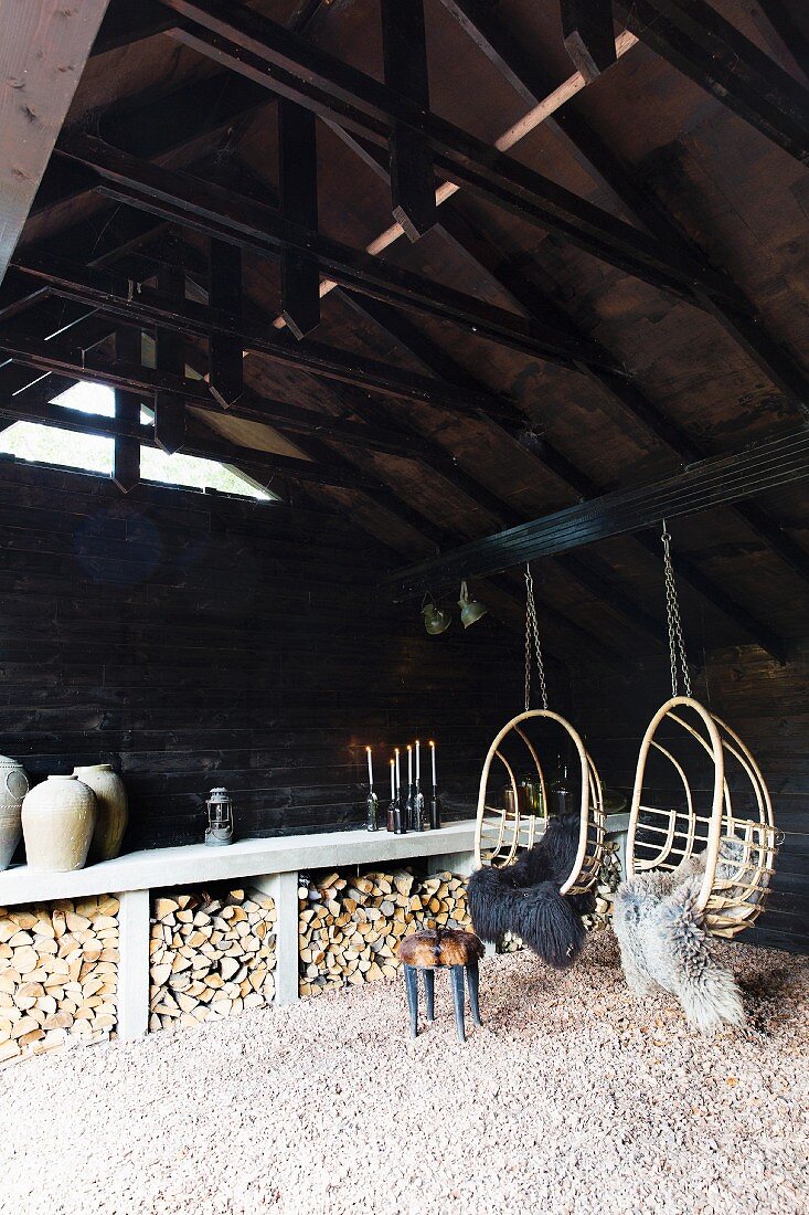 Zwei Korbhängesessel mit Schaffellen an Scheunenbalken aufgehängt; Holzlagerplatz an Scheunenwand