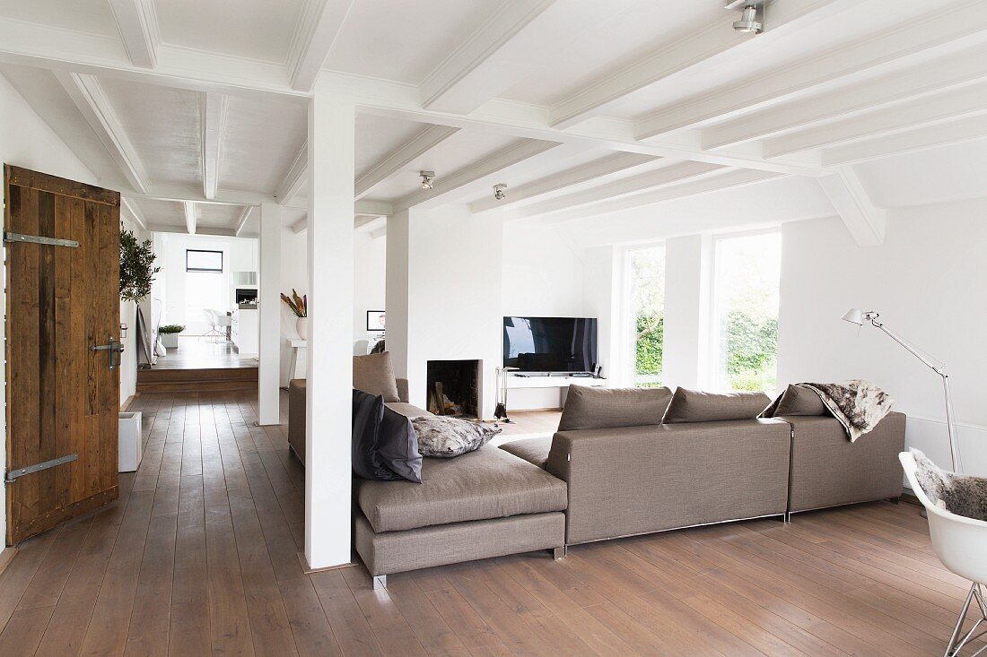 Elegante hellgraue Sofakombination in offenem Wohnraum mit ländlichem Charme, weiße Holzbalkendecke und Stützenkonstruktion
