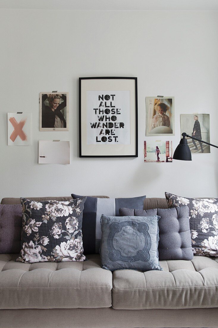 Patterned scatter cushions in shades of grey on beige sofa below collage of pictures on wall