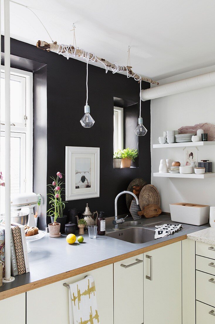 weiße Küchenzeile vor schwarzer Wand mit Fenstern und kreativer Beleuchtung