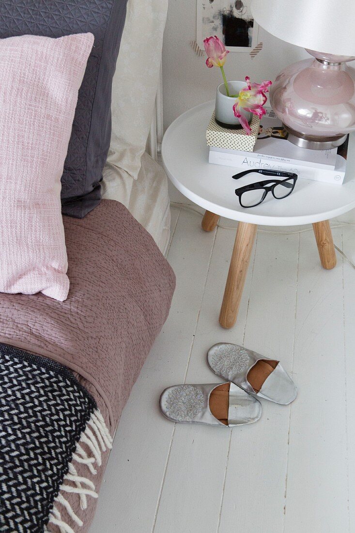 Slippers next to bedside table with table lamp and black spectacles