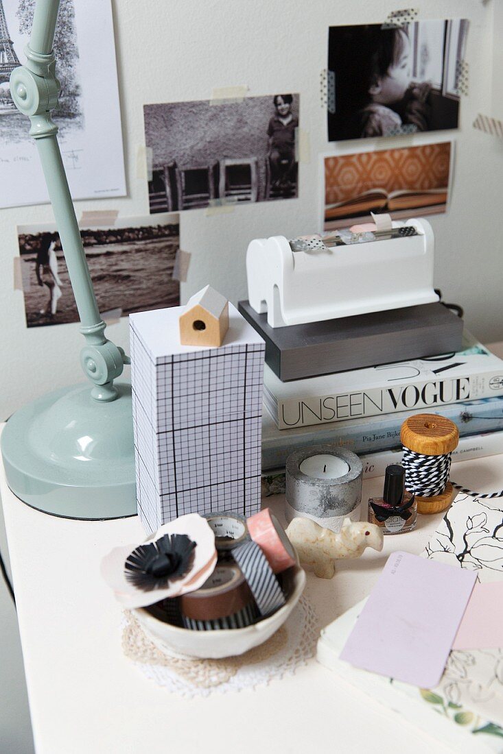 Klebebänder in Schale und Notizzettel neben Bücherstapel auf Schreibtisch, Fotos mit Masking Tapes an Wand geklebt
