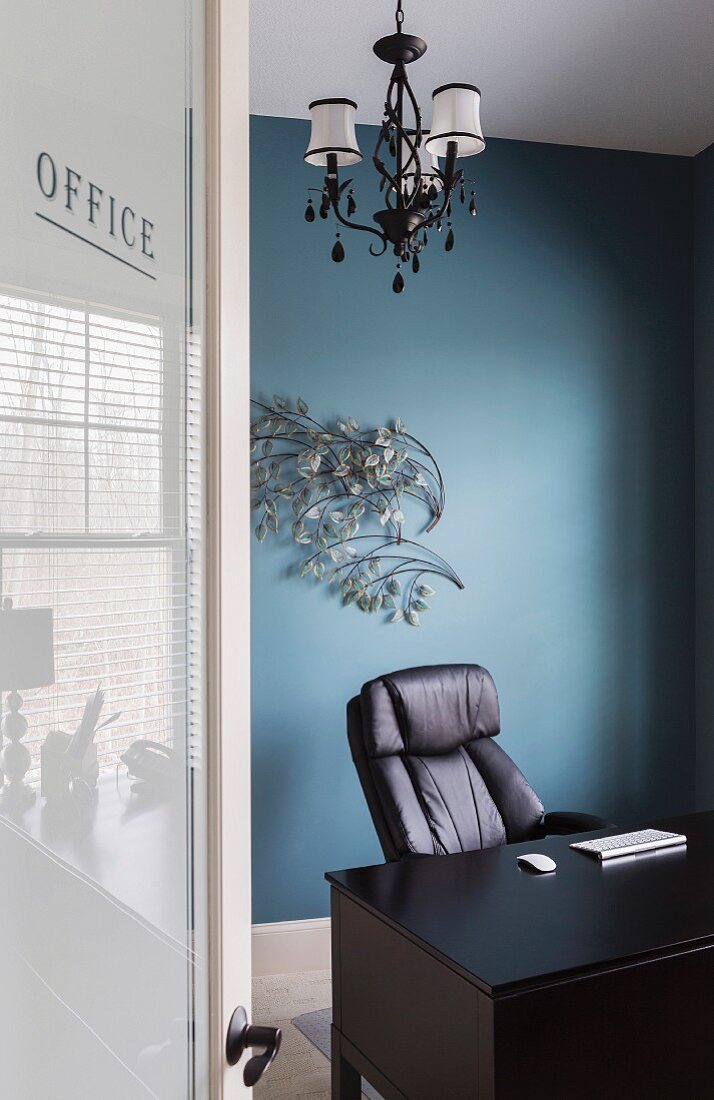 Home Office mit blauer Wand, davor ein Schreibtisch und ein schwarzer Lederstuhl