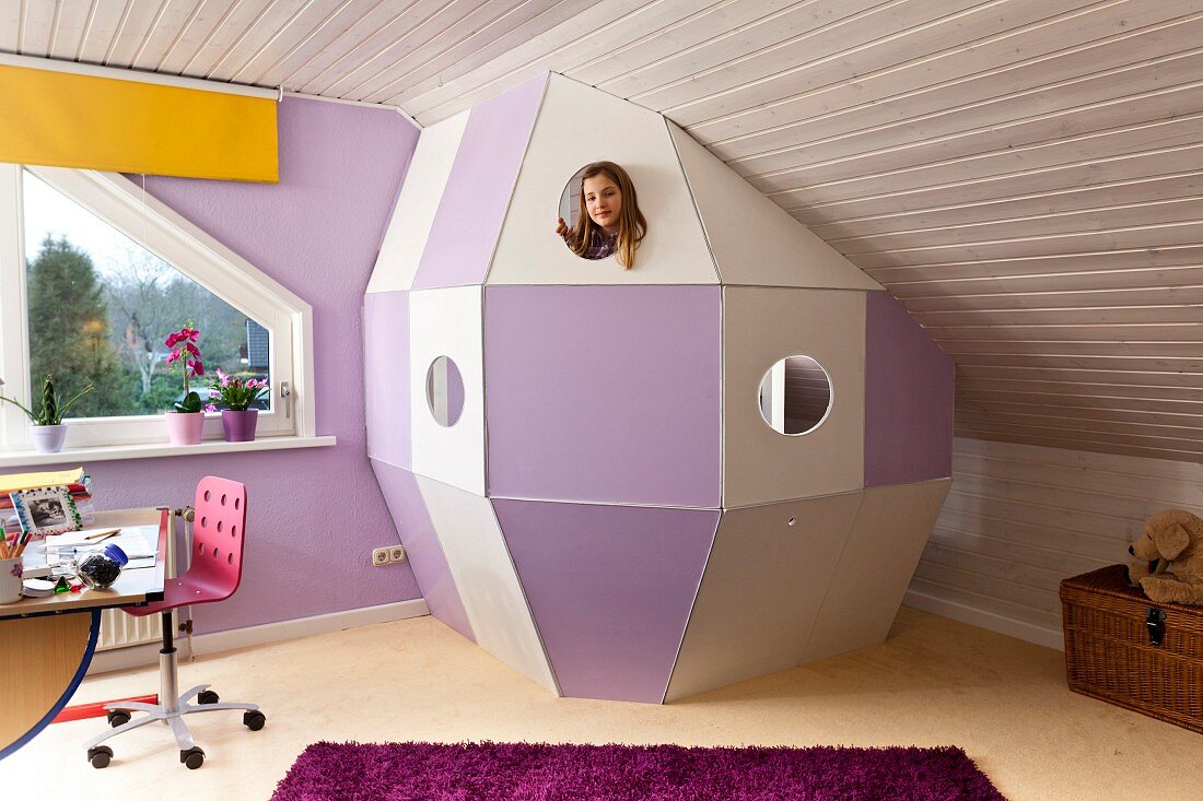 Selbstgebaute Raumkapsel aus weissen und violetten Holzpaneelen, unter Dachschräge im Kinderzimmer, Mädchen hinter Guckloch